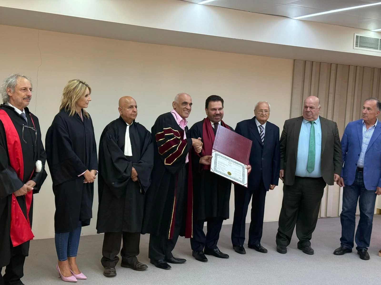A graduate receiving a diploma from faculty members in academic gowns